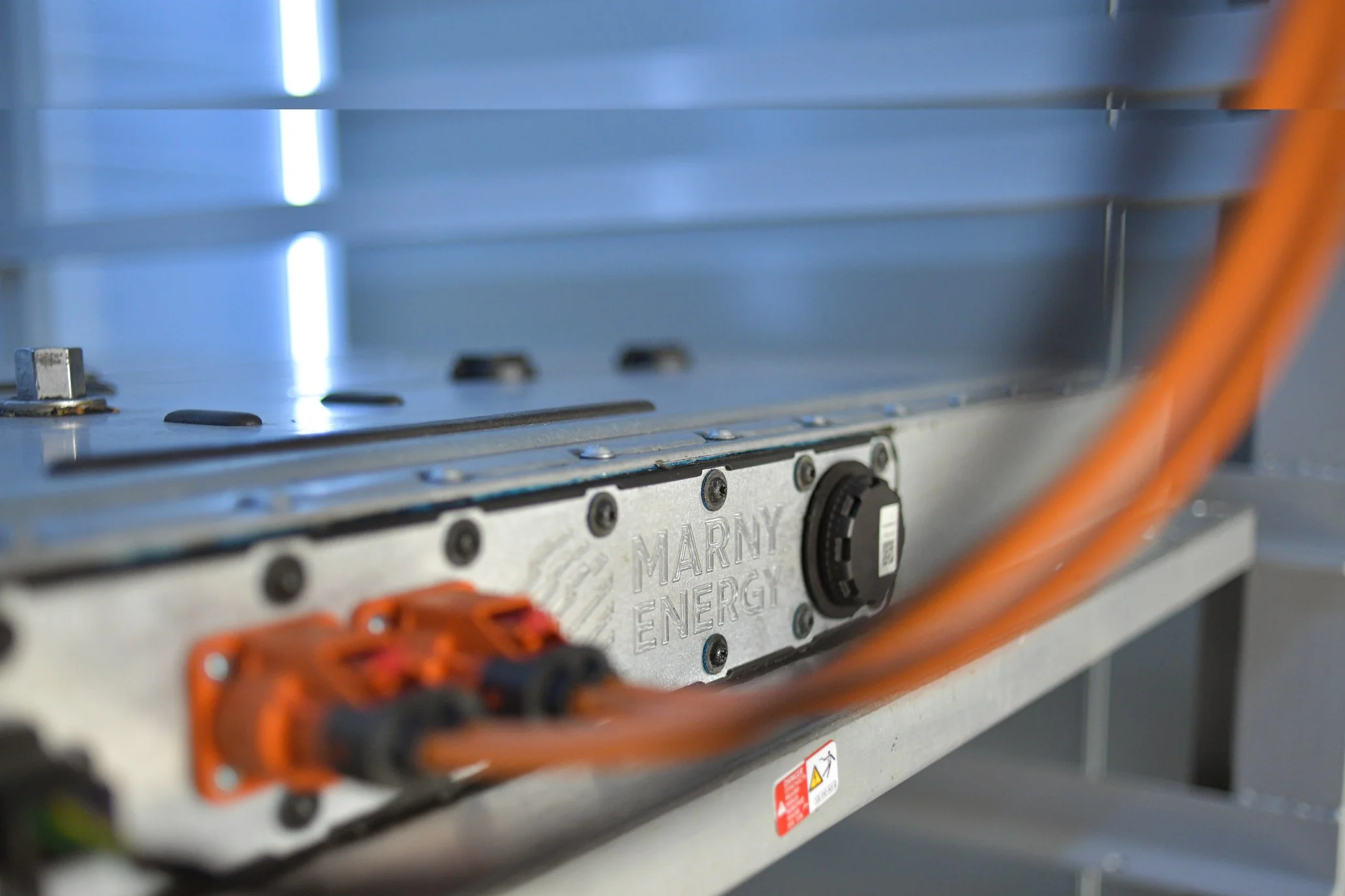 Gros plan sur un module de batterie de seconde vie, issu d’un véhicule électrique, logo MARNY ENERGY en relief dans le métal et câblage haute tension orange